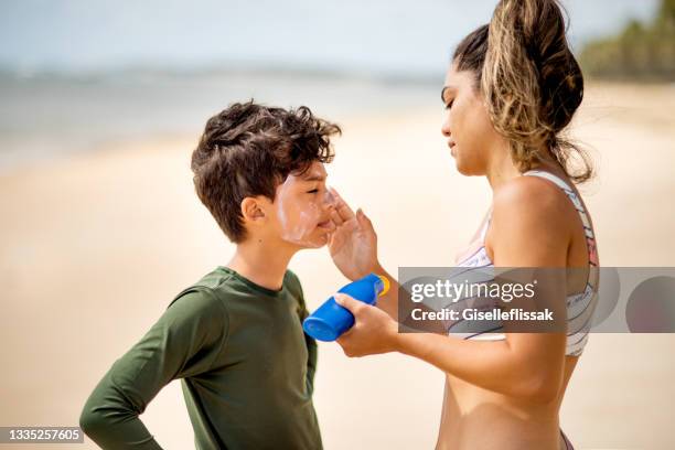 mãe colocando loção bronzeante no rosto do filho na praia - protetor solar - fotografias e filmes do acervo