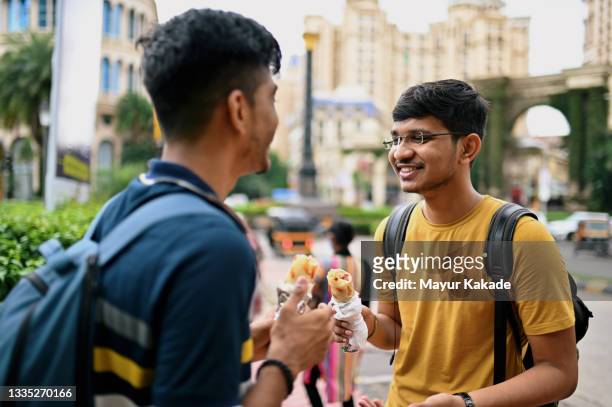 two young men standing on a city street and eating taco - asian eating hotdog stock pictures, royalty-free photos & images