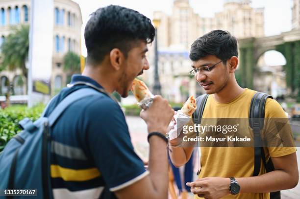 two young men standing on a city street and eating taco - asian eating hotdog stockfoto's en -beelden
