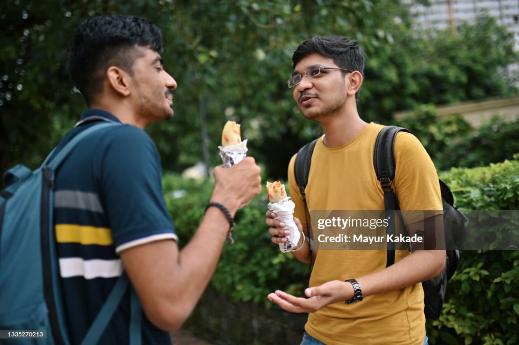 Two young men standing on a city street and eating taco