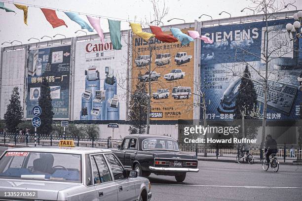 View of billboards lining an unspecified street, Beijing, China, April 1986. The ads include promotions for Canon computers, Nissan cars, and Siemens...