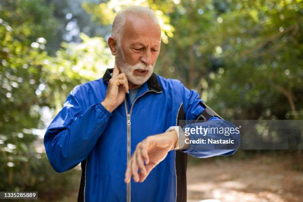 senior man taking a break measuring pulse - running man heartbeat stock pictures, royalty-free photos & images