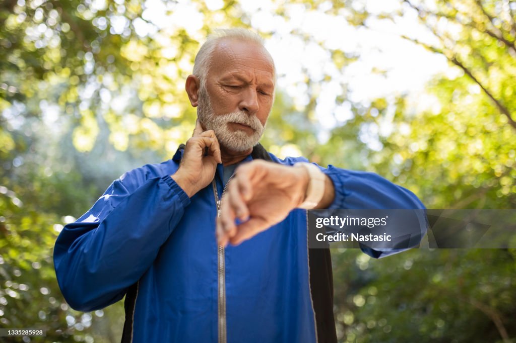 Senior Man Jogging taking a break measuring pulse
