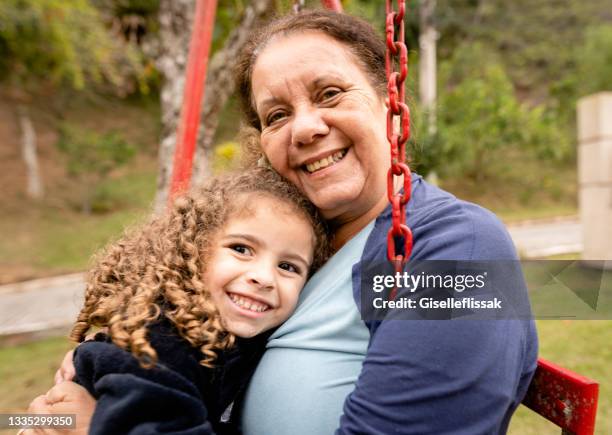 femme âgée souriante et sa petite-fille assise sur une balançoire - family garden play area photos et images de collection