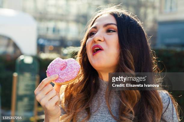 young woman eating a donut - mastigar imagens e fotografias de stock