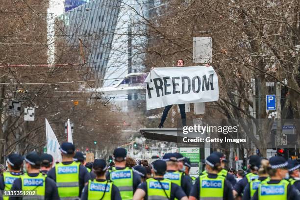 Man holds a banner reading "Freedom" atop a tram stop during an anti-lockdown protest on August 21, 2021 in Melbourne, Australia. Anti-lockdown...