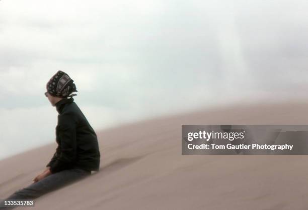 young woman sitting on sand dune on windy day - foulard vent photos et images de collection