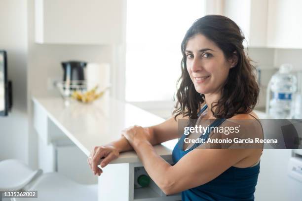 woman in sportswear poses smiling in the kitchen of her home - smirking stock pictures, royalty-free photos & images