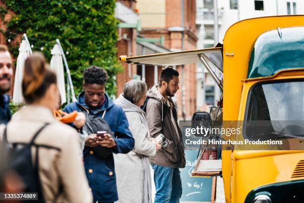 man ordering at food truck with other people waiting in line - furgone ambulante foto e immagini stock