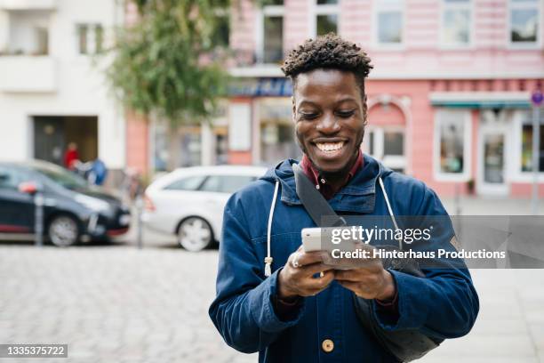 man smiling while using smartphone - unkompliziert stock-fotos und bilder