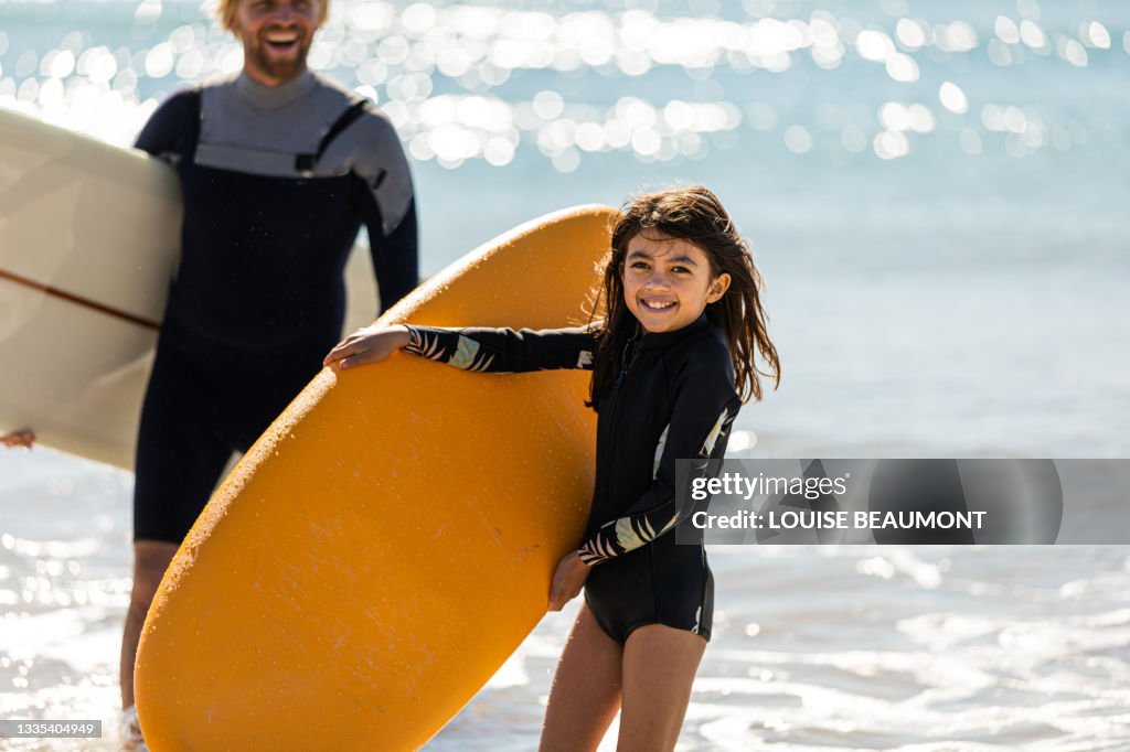 Surfing dad and daughter carry their boards from the surf