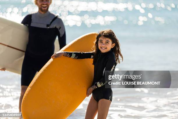 surfing dad and daughter carry their boards from the surf - real world stock pictures, royalty-free photos & images
