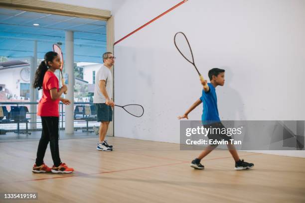 asian squash coach practicing with his 2 students at squash court together showing serving method - racket ball stock pictures, royalty-free photos & images