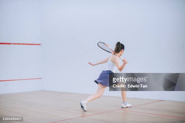 rückansicht asiatisches chinesisches teenager-mädchen, das allein auf dem platz squash spielt - squash racquet stock-fotos und bilder