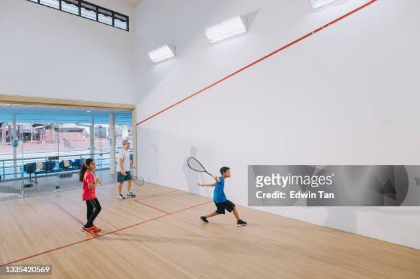 wide shot asian squash coach practicing with his 2 students at squash court together showing serving method - squash racquet stockfoto's en -beelden