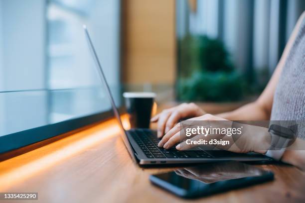 close up of businesswoman typing on keypad on laptop in a contemporary office space, with smartphone and a cup of coffee by her side. lifestyle and technology. staying connected throughout the city. business on the go - アクセス ストックフォトと画像