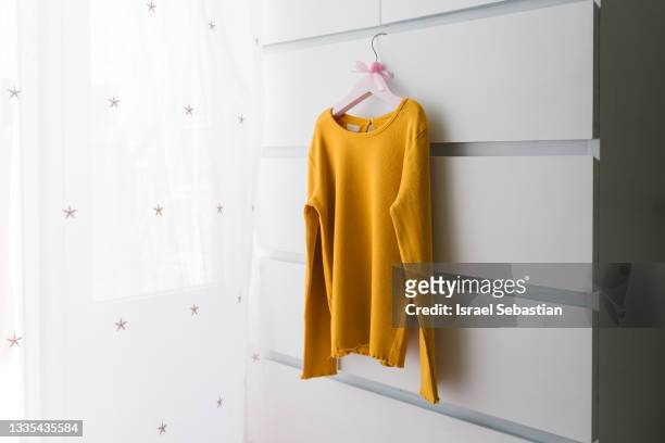close up shot of a minimalist image of a yellow sweater hanging on a hanger on a white background. - maglione foto e immagini stock