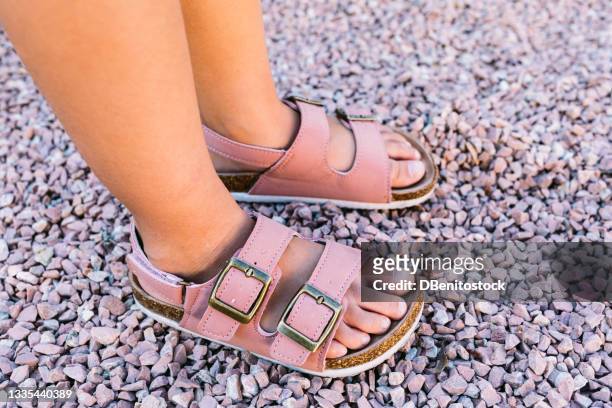 closeup side view of toddler girl feet wearing pink buckle sandals on pink stones in natural light with hard shadows - sandales photos et images de collection