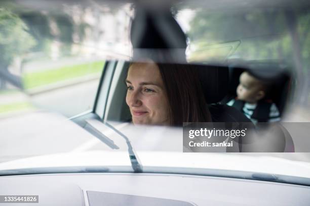 beautiful smiling woman driving a car with little baby on the backseat - rear view mirror stock pictures, royalty-free photos & images