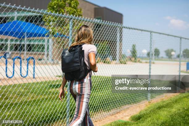 teenager-mädchen, das vor dem öffentlichen schulgebäude neben der zaunbarriere geht zurück zur schule fotoserie - sekundarschule stock-fotos und bilder