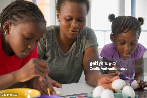 afroamerikanische mutter und töchter malen eier für ostern am wohnzimmertisch - temperamalerei stock-fotos und bilder