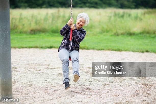 seniorin auf schaukel auf dem spielplatz - grey hair cool woman stock-fotos und bilder