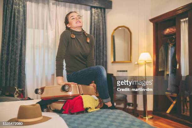woman struggling with overflowing suitcase - stuffing imagens e fotografias de stock