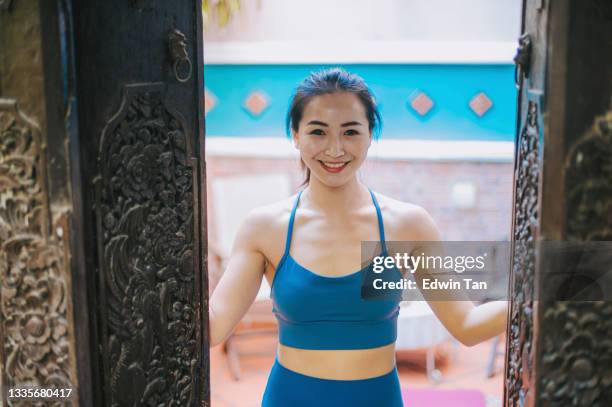 asian chinese beautiful woman with sport clothing outfit open wooden door looking at camera with toothy smile happy - open workouts imagens e fotografias de stock