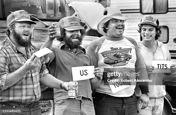 Fans harass a woman with "Show us your tits" signs as she walks past them in the speedway infield during the running of 1984 Firecracker 400 race at...