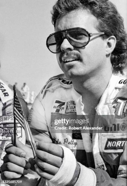 Driver Kyle Petty holds a small U.S. Flag during drivers introductions prior to the start of the 1984 Firecracker 400 race at Daytona International...