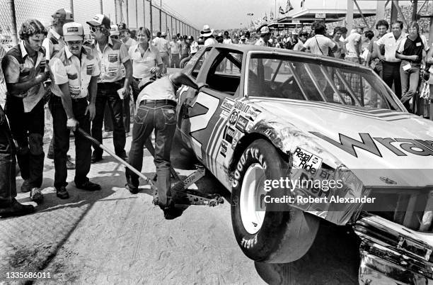 Driver Dale Earnhardt Sr. Sits in his racecar as member sof his racing team work on his damaged racecar during the running of the 1981 Firecracker...