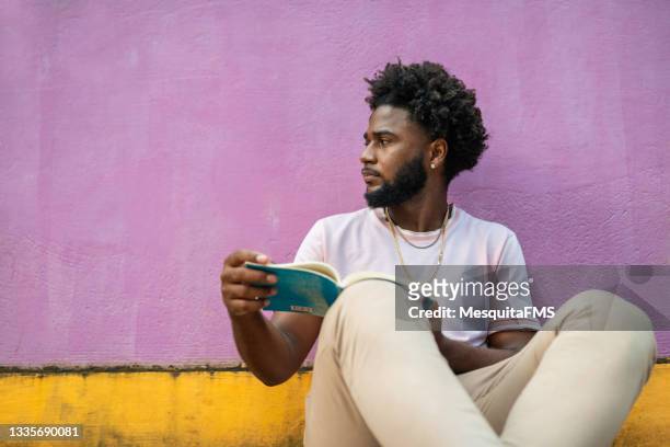 afro-mann sitzt auf dem boden und liest buch - zweifarbig farbe stock-fotos und bilder