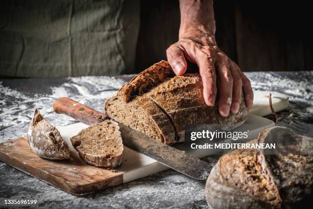 männliche hände schneiden sauerteigbrotscheiben vollkorn nach hausgemachter deutscher art auf schneidebrett - loaf of bread stock-fotos und bilder