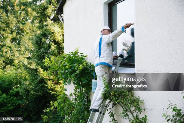 house painter paints the window frame from the outside - huisschilder stockfoto's en -beelden
