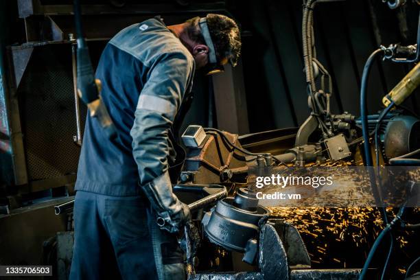 male worker using grinder to clean surface of product, stream of hot and bright sparks - smeden stockfoto's en -beelden