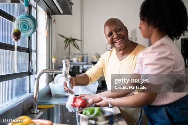 grandmother and granddaughter washing vegetables together at home - food waste stockfoto's en -beelden