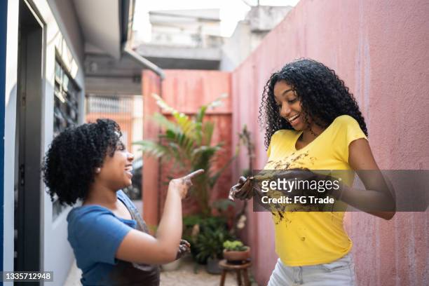 sisters wiping messy hands on shirt after planting flower at home - stained shirt stock pictures, royalty-free photos & images