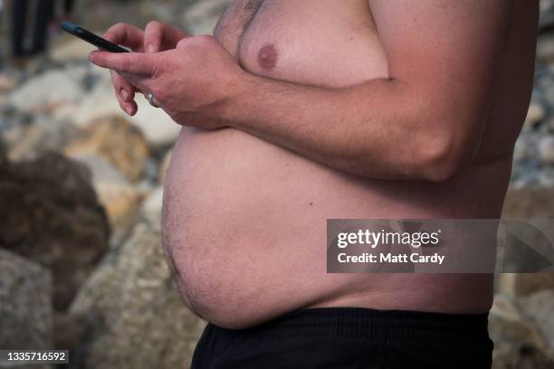 Topless man looks at his phone at Sennen Cove on August 20, 2021 near Penzance in Cornwall, England. The ongoing international travel restrictions...