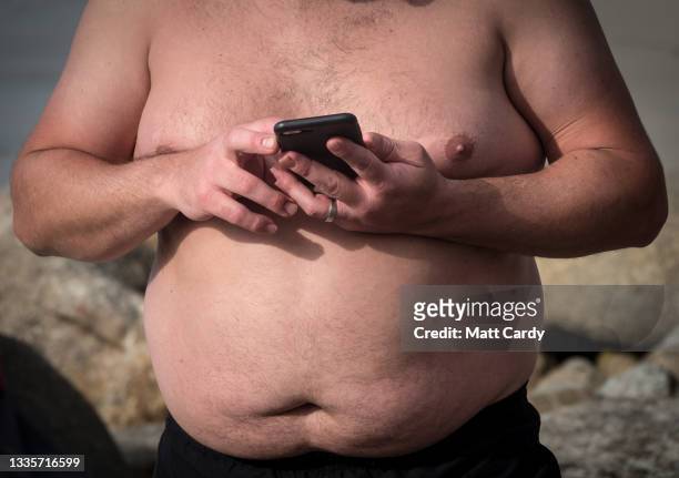 Topless man looks at his phone at Sennen Cove on August 20, 2021 near Penzance in Cornwall, England. The ongoing international travel restrictions...