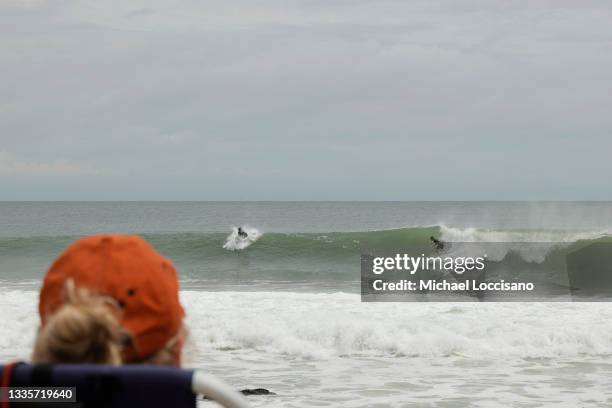 Woman watches from the beach as one surfer rides a wave that another contemplates dropping in on on August 22 in Bay Head, New Jersey. Heavy rains...