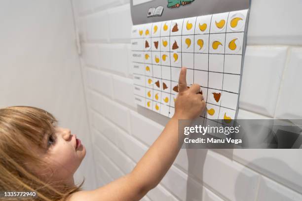 cropped view of a cute blonde little girl looking and pointing at her pee and poop calendar on which she has stuck stickers on the days on which she performed each action. - childrens closet stockfoto's en -beelden