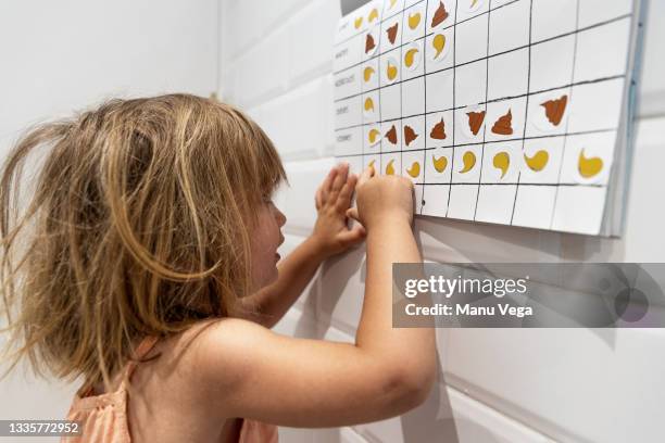 female child sticking stickers of pees and poops on calendar on the days where she has done each action. - childrens closet stockfoto's en -beelden
