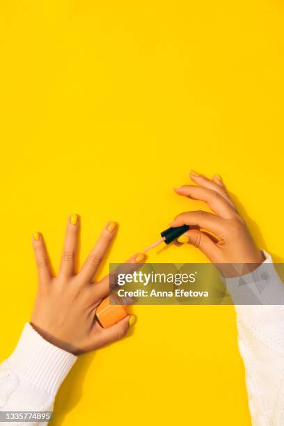 woman paints her fingernails with orange nail polish on yellow background. she is wearing a white sweater. concept of domestic life. flat lay style - painting fingernails stock pictures, royalty-free photos & images