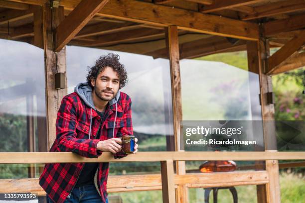 latino man is on the balcony of his country house with a cup of coffee in his hands while looking at the landscape - colombian coffee mountain stock pictures, royalty-free photos & images