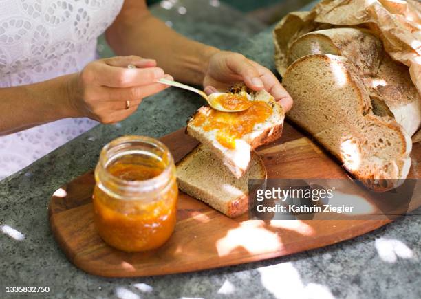 woman spreading apricot jam on fresh bread, close-up of hands - preserves stockfoto's en -beelden