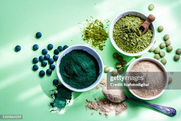 spirulina, maca und moringa pulver und pillen auf grünem hintergrund - superfood stock-fotos und bilder