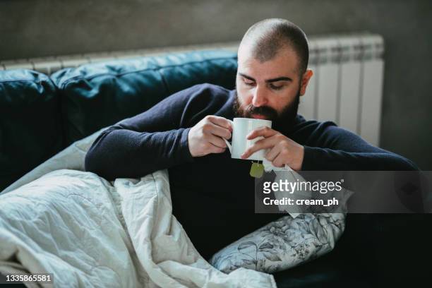 sick man drinking tea in bed and holding a paper tissue - man having tea stock pictures, royalty-free photos & images