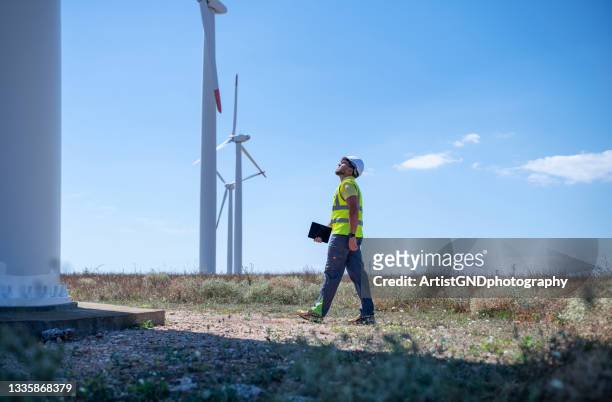 technician walking to the base of a wind turbine with digital tablet - mill worker stock pictures, royalty-free photos & images