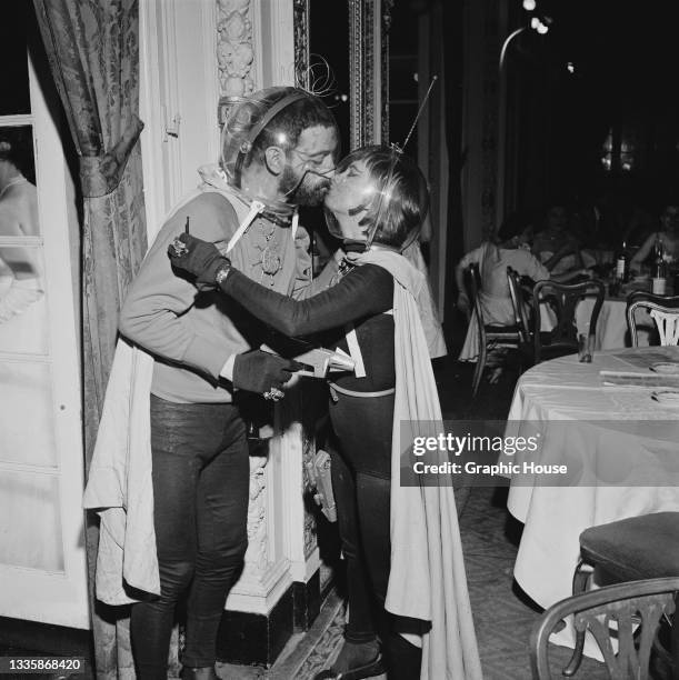 Guests wearing costumes with space helmets 'kiss' at the Artists' Equity Masquerade Ball, held at the Hotel Sheraton Astor in the borough of...