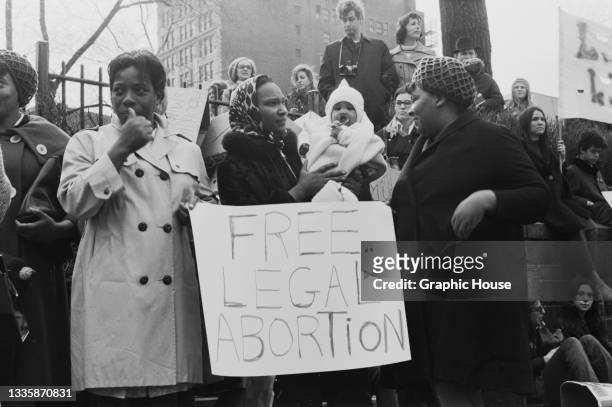 Protestors, one holding a child, stand around a placard reading 'Free legal abortion' during a mass demonstration against New York State abortion...